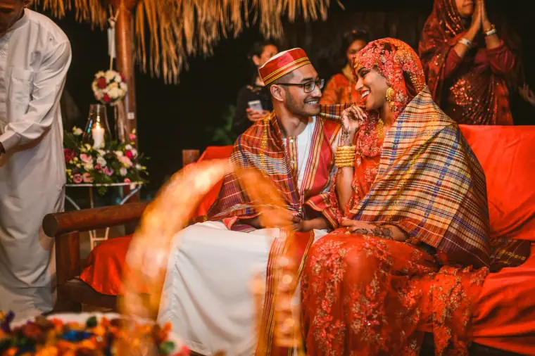 Bride and groom laughing on a red daybed, draped in a tartan shawl