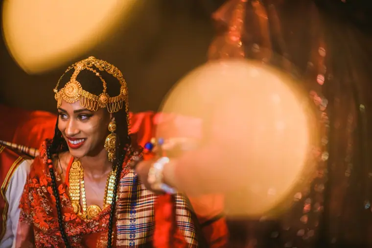 Bride in a gold headdress smiling, framed by glowing bokeh lights