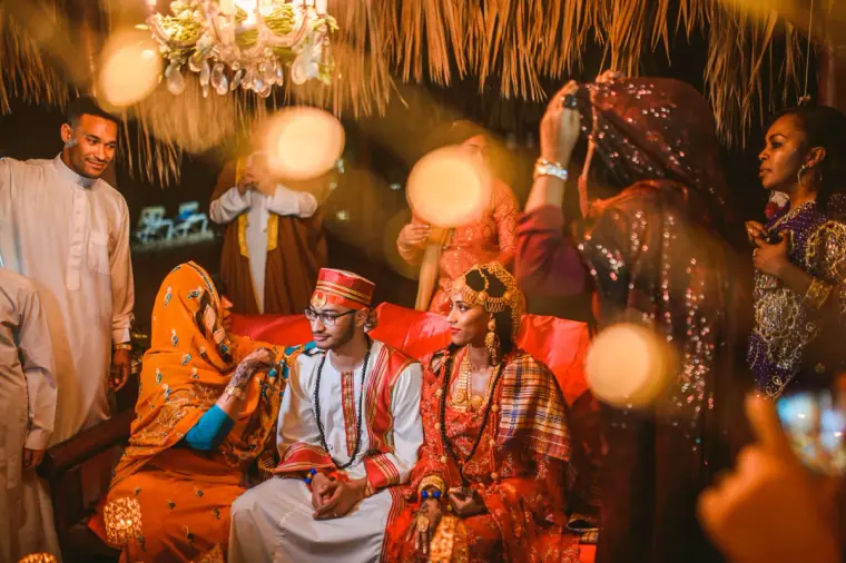 Couple seated on the daybed as guests surround them under the chandelier at night