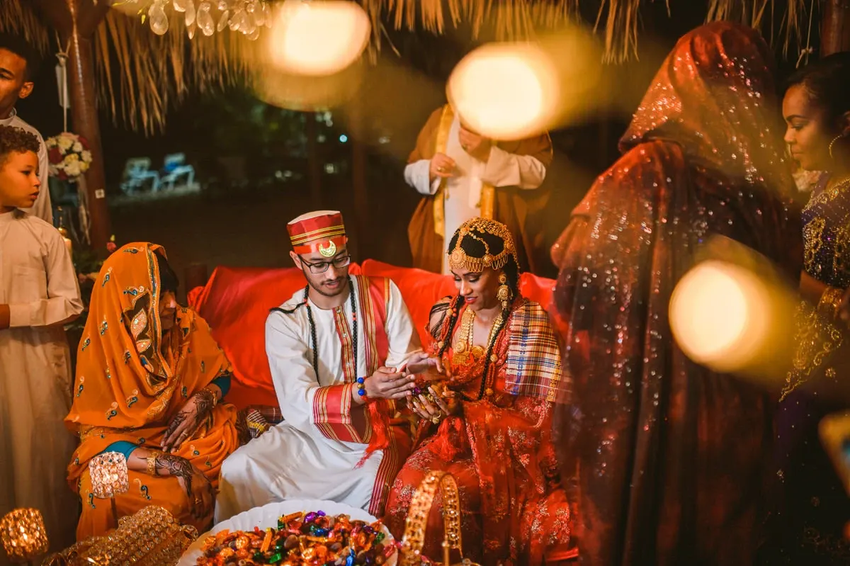 Bride and groom on the red daybed during the evening ceremony, surrounded by relatives and bokeh lights