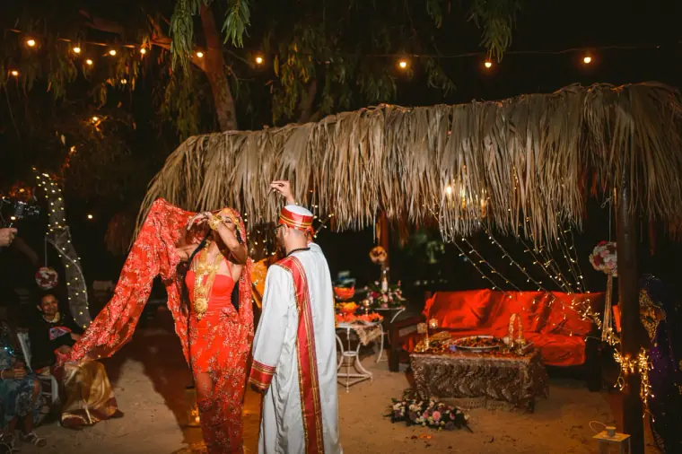 Bride in red performing a traditional dance as the groom watches under the canopy