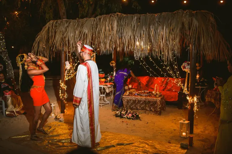 Bride in a short red dress dancing before the groom in his white robe and red cap