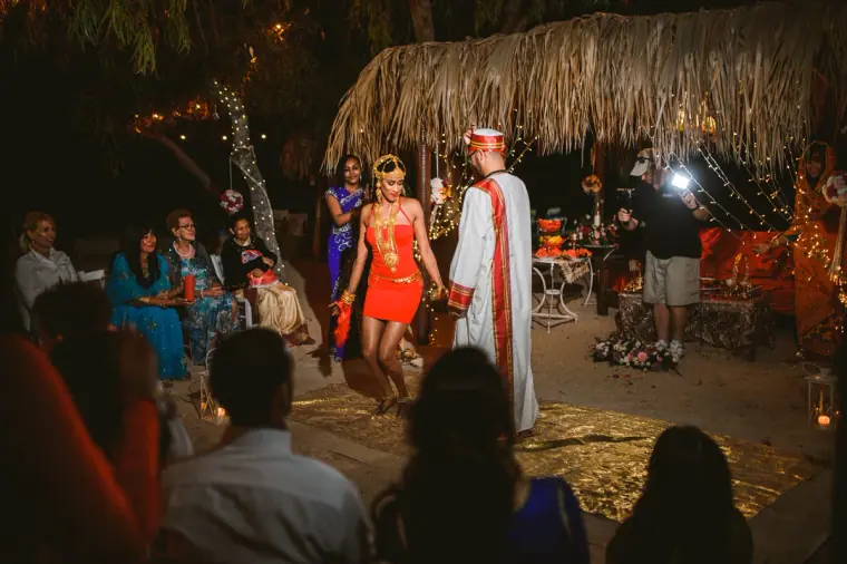 Guests watching the bride dance for the groom beneath the thatched canopy at night