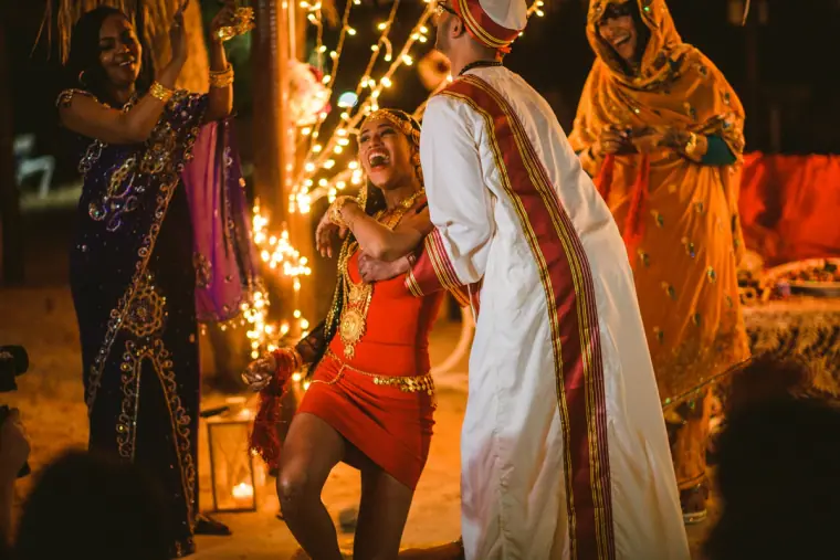 Bride in red dancing beside the groom as women in saris clap along