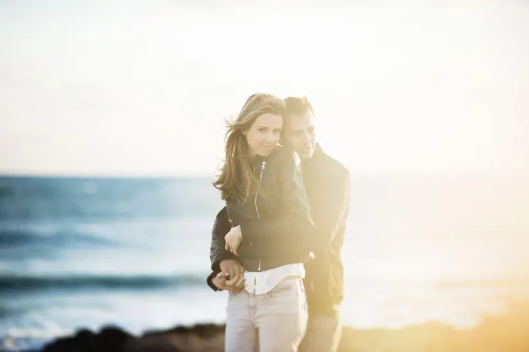 Joanna and Andrew cuddling by the sea in soft, hazy sunset light, Paphos