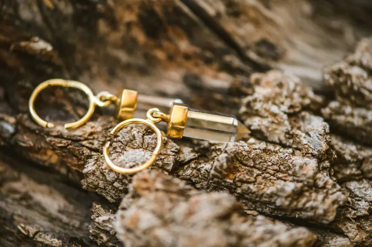 Gold drop earrings resting on weathered tree bark