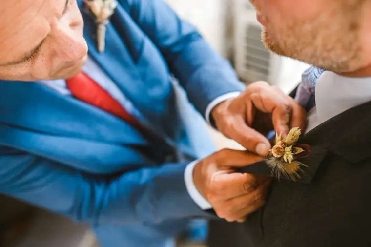 Close-up of hands pinning a dried-flower buttonhole to a grey jacket