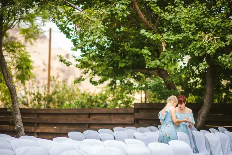Bridesmaids in blue standing behind rows of white ceremony chairs under trees