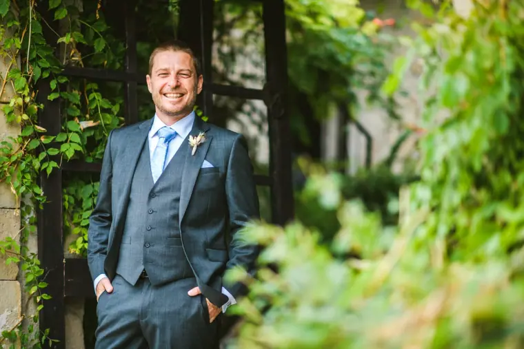 Kazem in a grey suit and blue tie, hands in pockets, among vines at Vasilias Nikoklis Inn