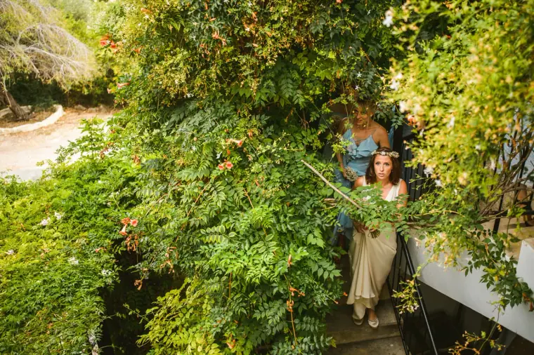 Bride walking down stone steps through flowering greenery with her bridesmaids