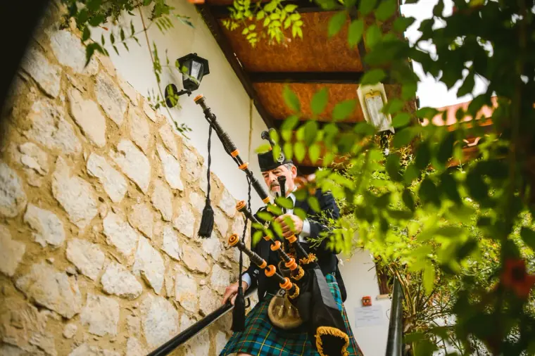 Bagpiper in a kilt playing at the top of stone steps beside the inn