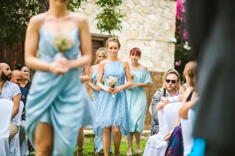 Bridesmaids in pale blue walking down the garden aisle holding small bouquets