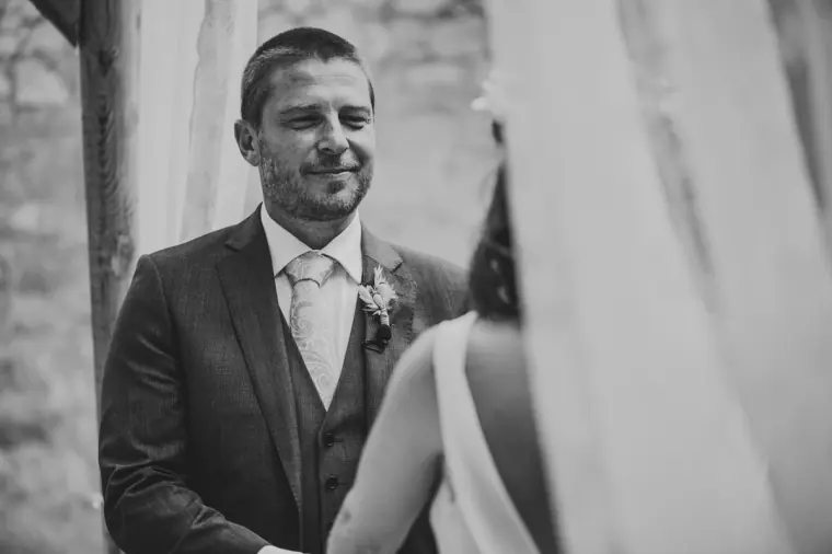 Black-and-white photo of the groom smiling at the bride at the altar