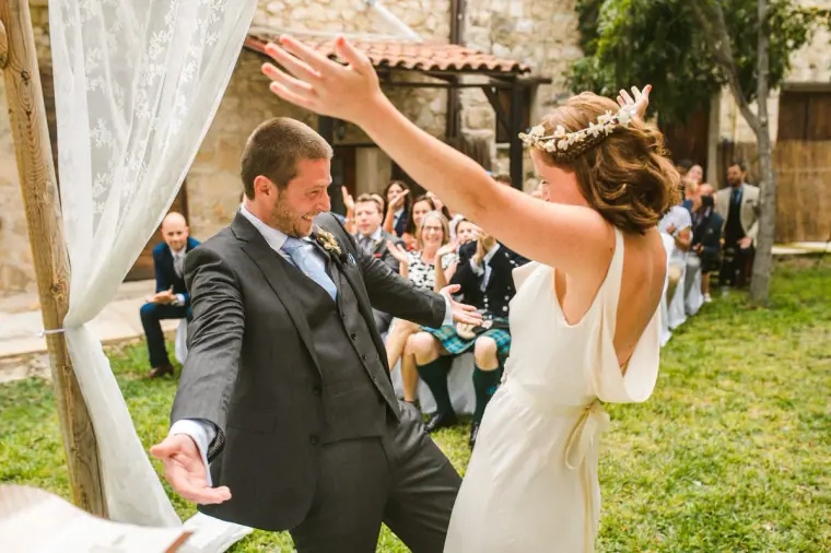 Bride cheering with arms raised as the groom celebrates in front of guests