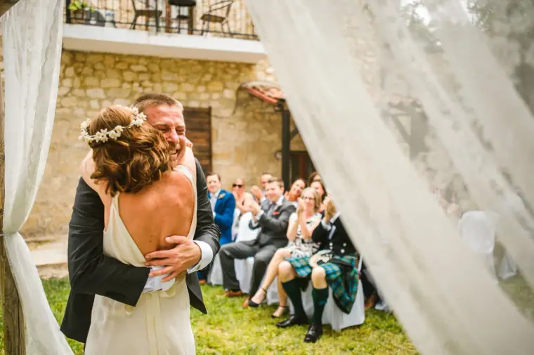 Bride and groom hugging beneath the lace-draped arch during the ceremony