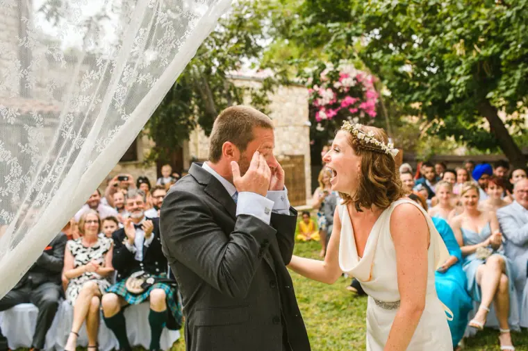Groom wiping away a tear as the bride laughs beside him