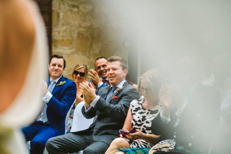 Guests in suits laughing and applauding during the ceremony