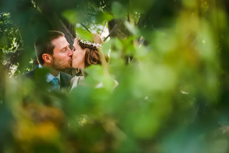 Fleur and Kazem kissing, framed by blurred green leaves