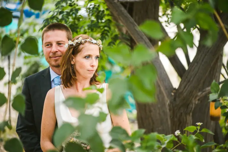 Groom and bride in a flower crown standing among olive branches