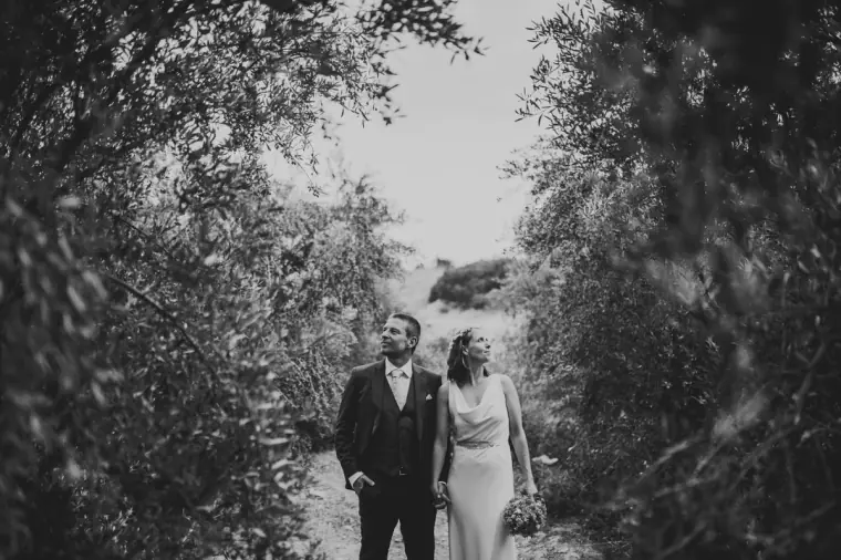 Black-and-white photo of bride and groom walking along a tree-lined track