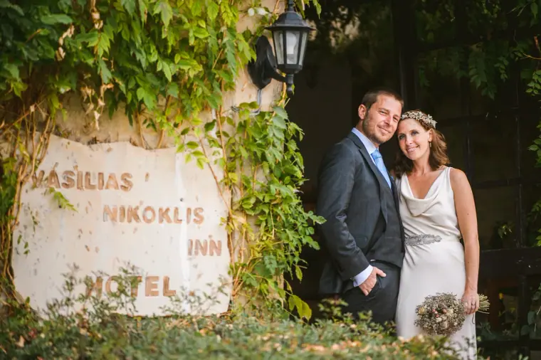 Bride and groom beside the vine-covered Vasilias Nikoklis Inn sign