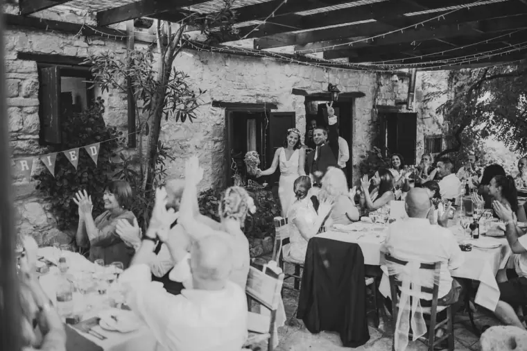 Black-and-white photo of guests raising a toast at the reception under the pergola