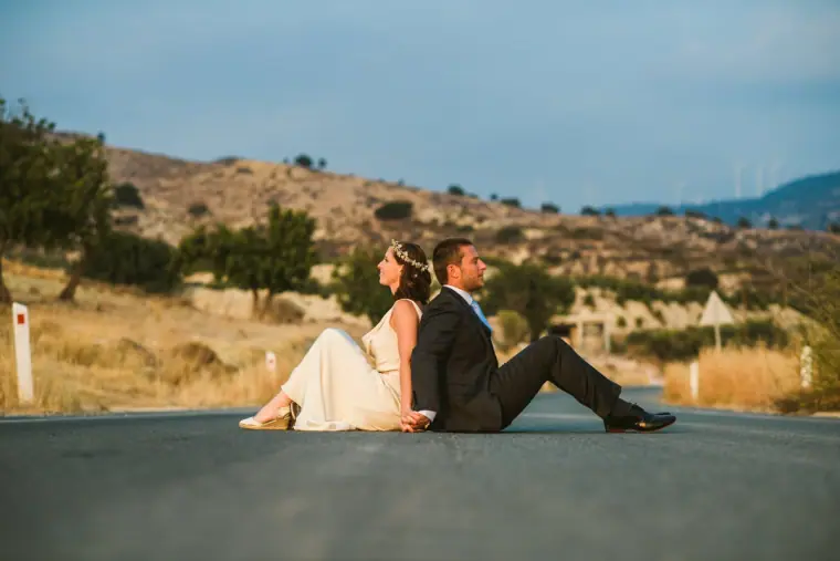 Bride and groom sitting back to back in the middle of a quiet country road