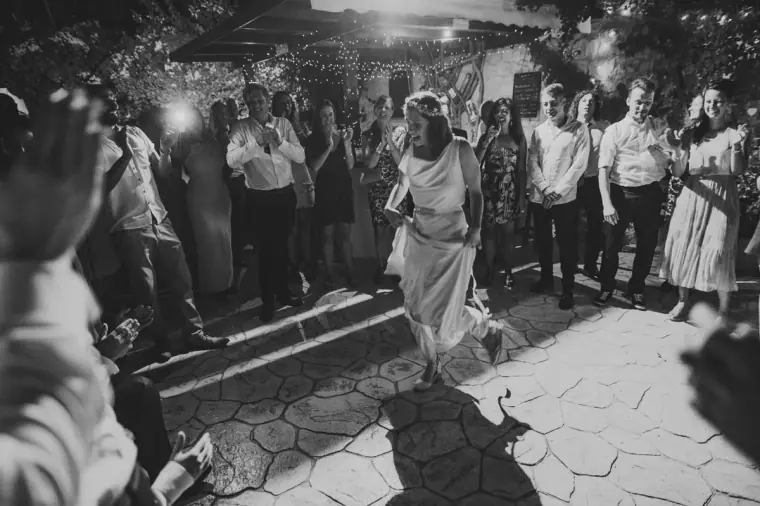 Black-and-white photo of the bride dancing as guests film on their phones
