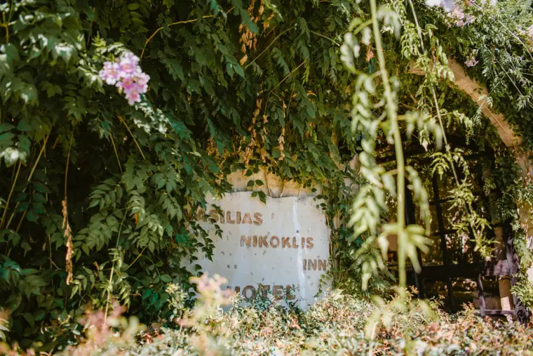 Vasilias Nikoklis Inn sign half hidden among greenery and pink blossom
