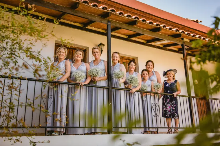 Bridesmaids in lilac grey with gypsophila bouquets lined up on the inn's balcony