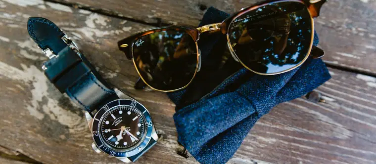 Watch, tortoiseshell sunglasses and a blue bow tie on a weathered wooden table