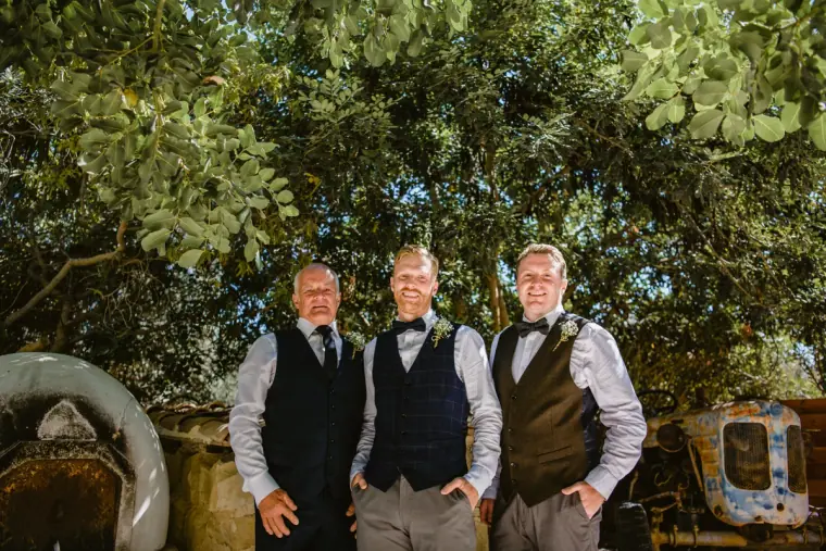 Groom and two groomsmen in waistcoats and bow ties standing in the garden