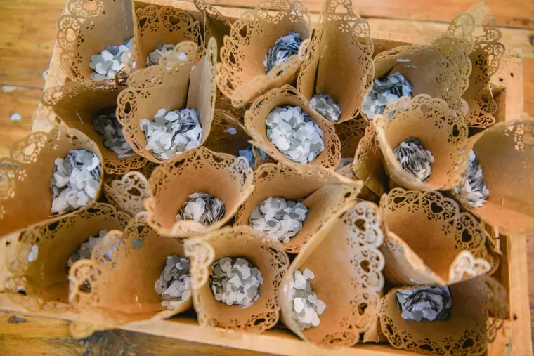Lace paper cones filled with dried petals for confetti in a wooden tray