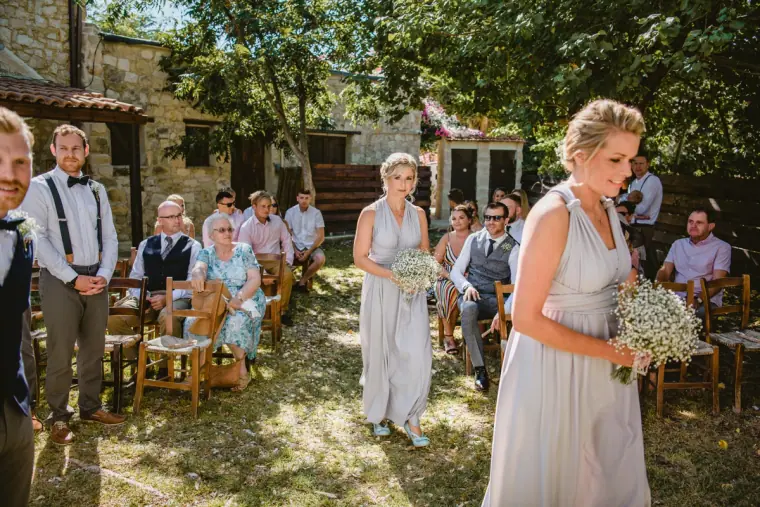 Bridesmaids walking down the aisle between seated guests in the courtyard