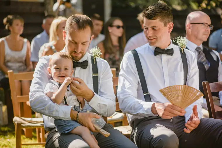 Guests in braces and bow ties watching the ceremony, one fanning himself