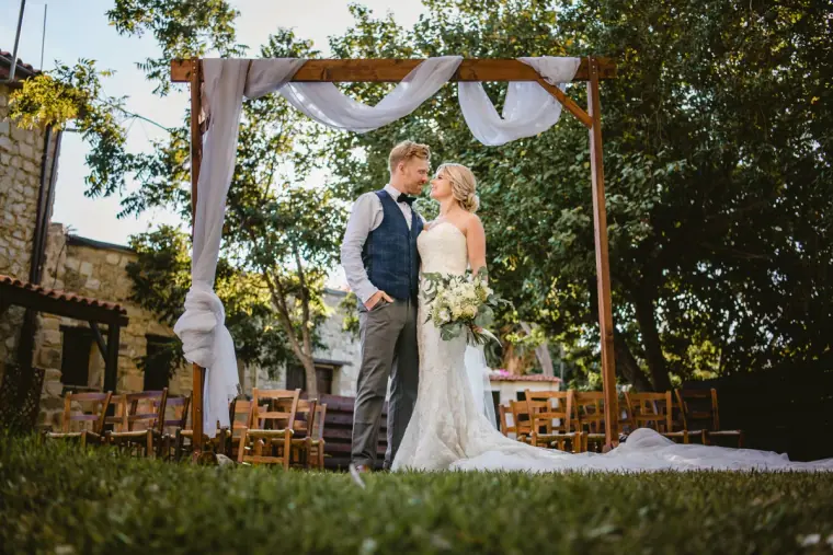 Bride and groom standing beneath the draped wooden ceremony arch