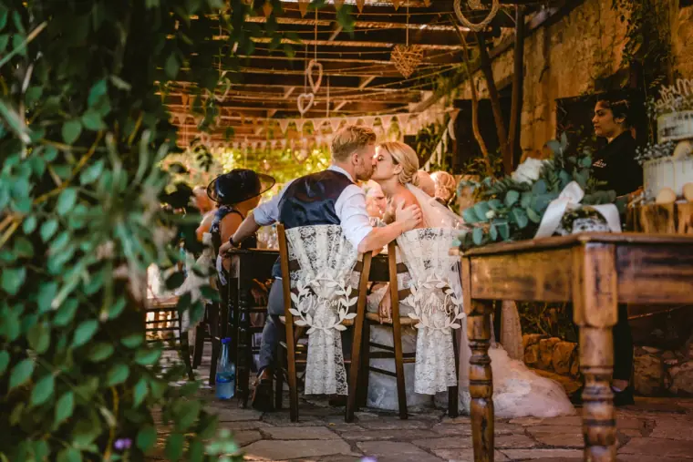 Bride and groom kissing at their lace-draped chairs on the vine-covered terrace