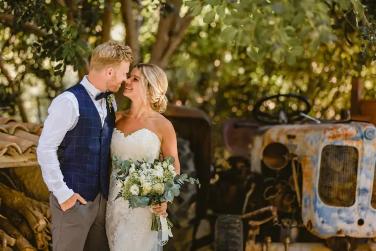 Groom kissing the bride's temple beside an old rusted tractor