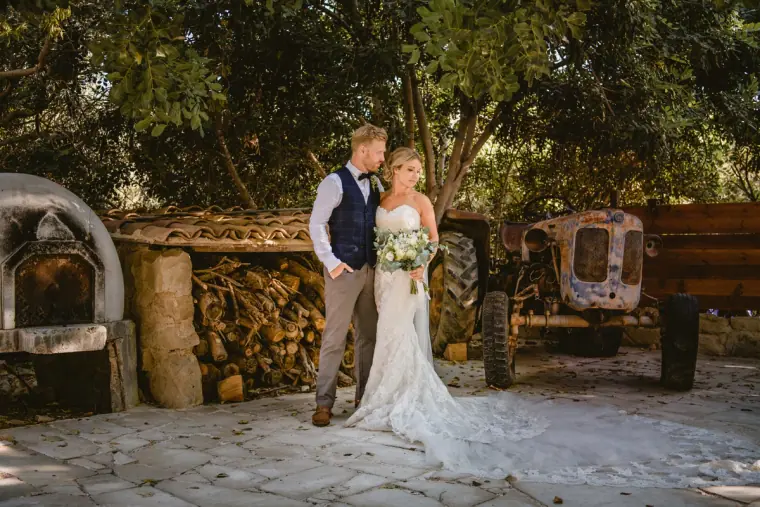 Bride and groom in the courtyard beside a stone oven and vintage tractor