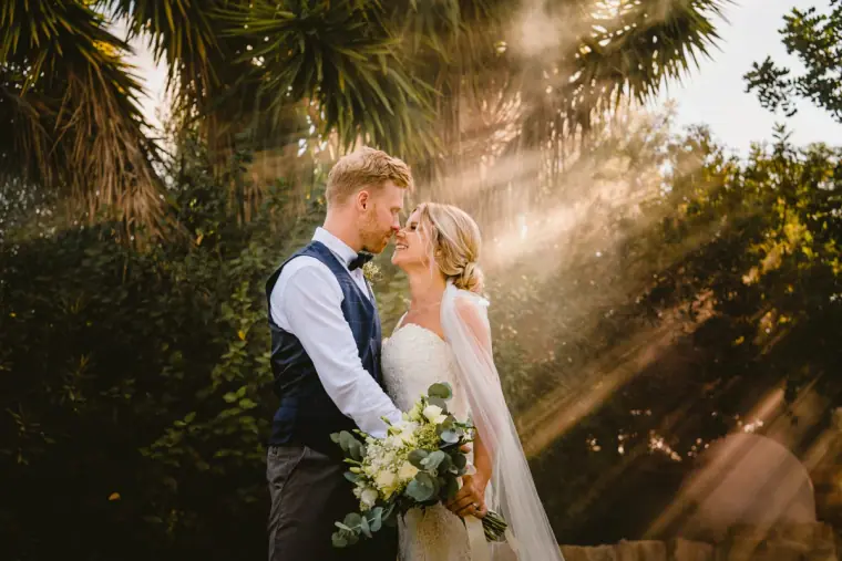 Paul kissing Fiona's forehead as sunbeams pour through the trees