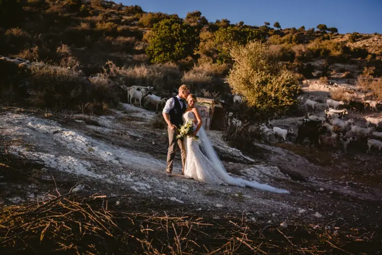 Fiona and Paul embracing on a rocky slope with a herd of goats behind