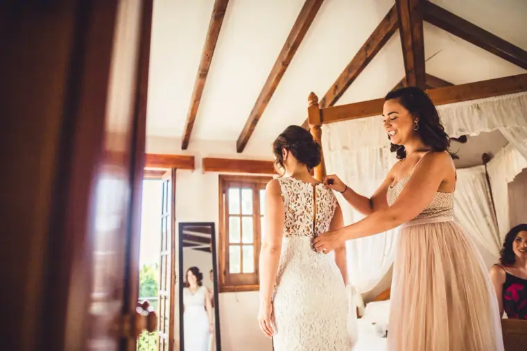 Bride being laced into her gown by a bridesmaid in blush tulle