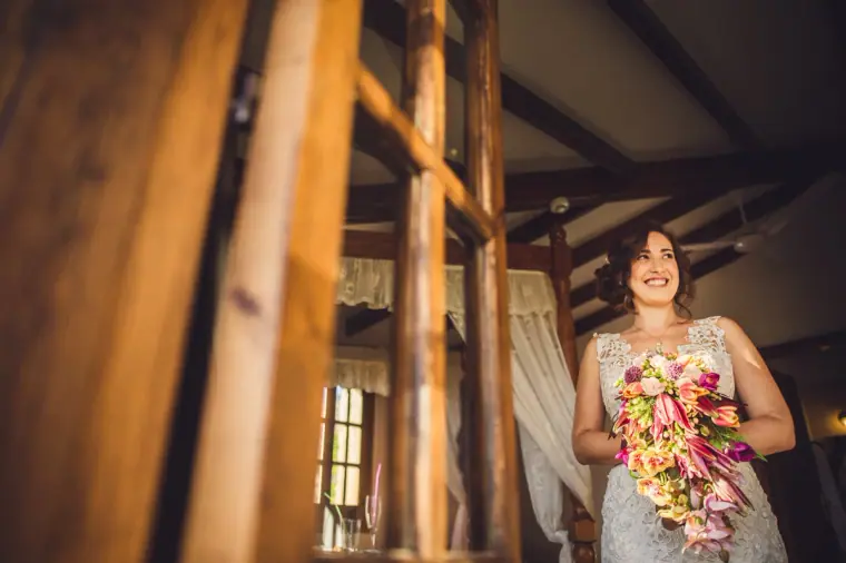 Bride holding a cascading tropical bouquet, framed by a wooden bed post