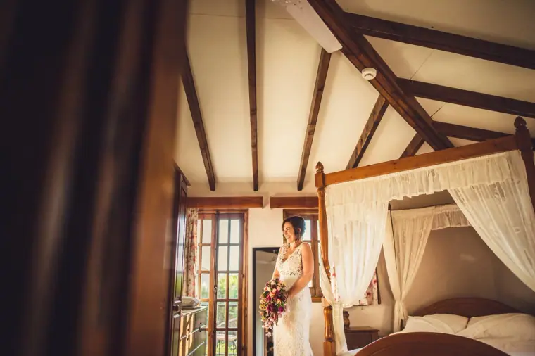 Bride standing by a four-poster bed in a beamed room at Vasilias Nikoklis Inn