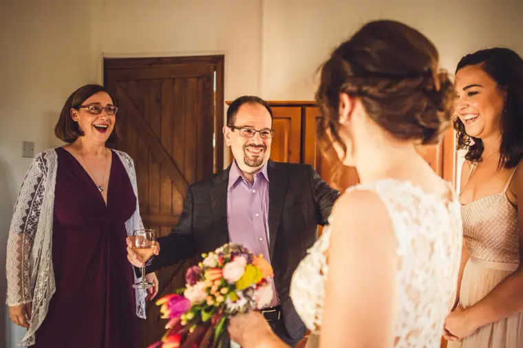 Bride with a colourful bouquet greeting smiling family members in the bedroom
