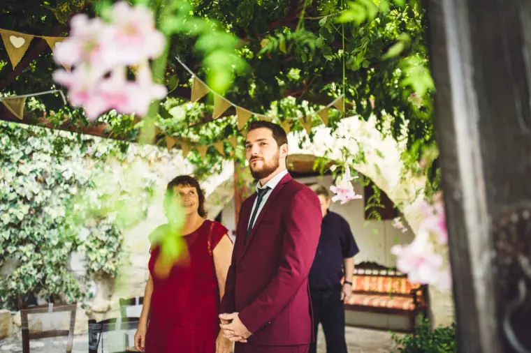 Groom in a burgundy suit waiting under the vine pergola at Vasilias Nikoklis Inn, Paphos
