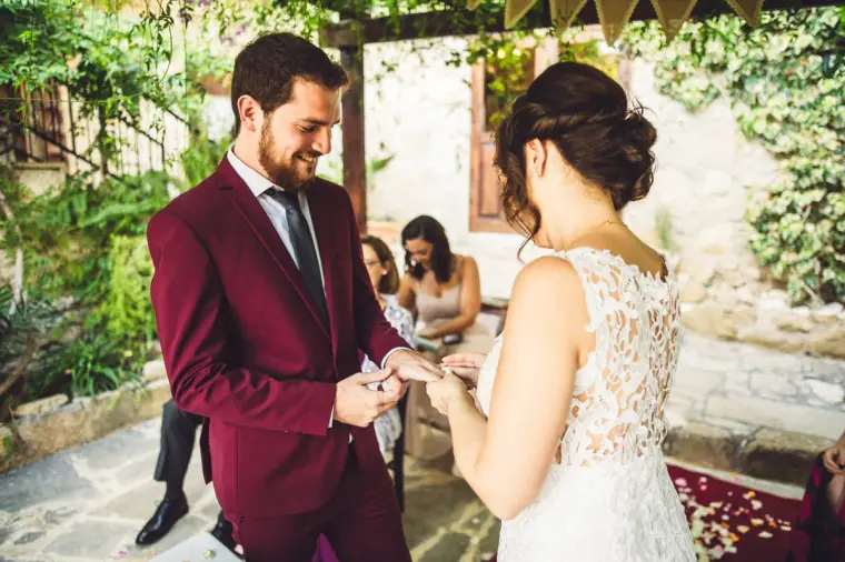 Groom placing the ring on the bride's finger in the stone courtyard