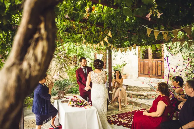 Couple exchanging vows under bunting and vines while seated guests look on
