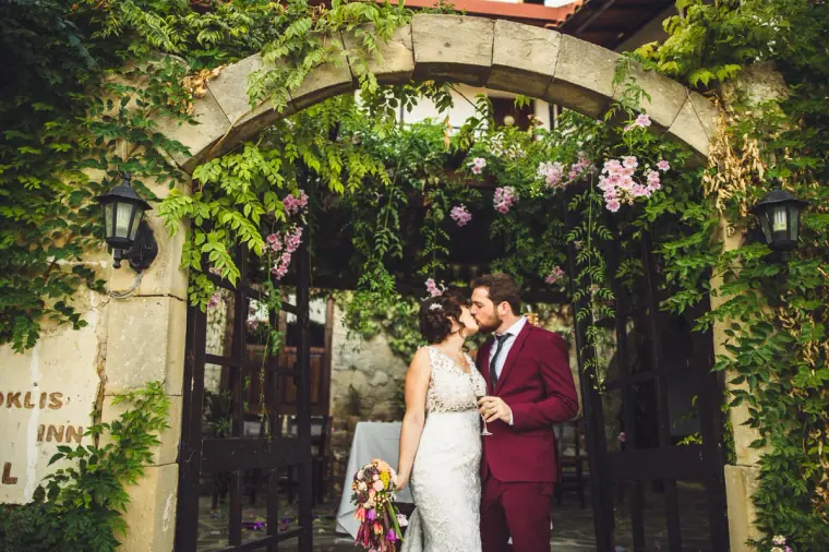 Bride and groom kissing beneath the flower-covered stone arch of the inn