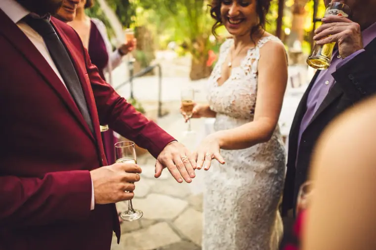 Groom and bride showing off her wedding ring as guests raise drinks